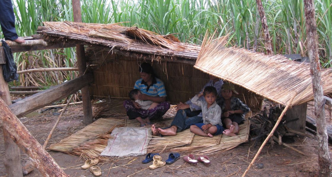 eine Familie mit drei Kindern sitzt unter einem Schilfdach