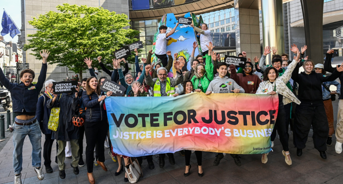 Eine Personengruppe springt in die Höhe und hält dabei ein Banner mit der Aufschrift "Vote for Justice" in die Höhe