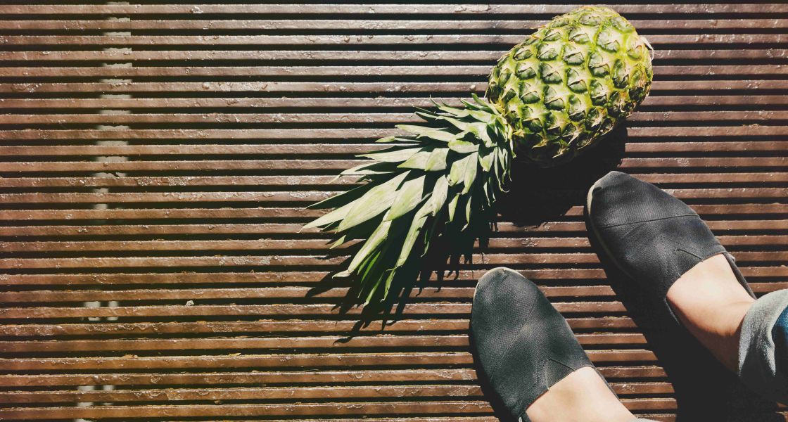 Eine Ananas liegt auf einem Holzfußboden und die Füße einer Person sind zu sehen