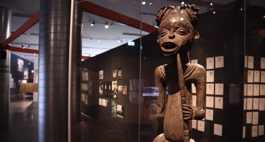 geschnitzte Holzfigur mit ausdruckstarkem Gesicht hinter einer Glasvitrine