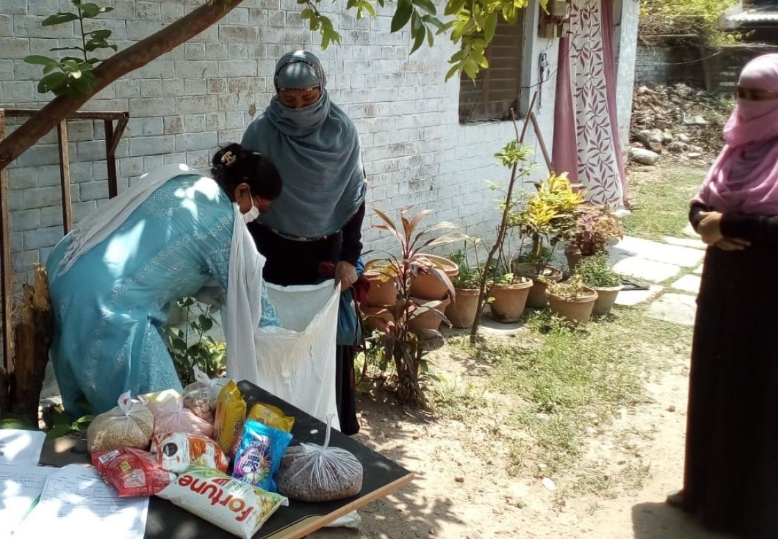 Eine indische Frau packt Lebensmittel in eine große weiße Tasche, die eine andere indische Frau in den Händen hält