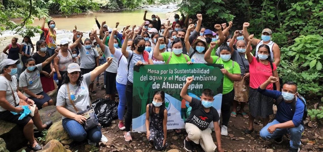 Viele Menschen, die die Fäuste hochheben, und mit einem Banner vor einem Fluss protestieren