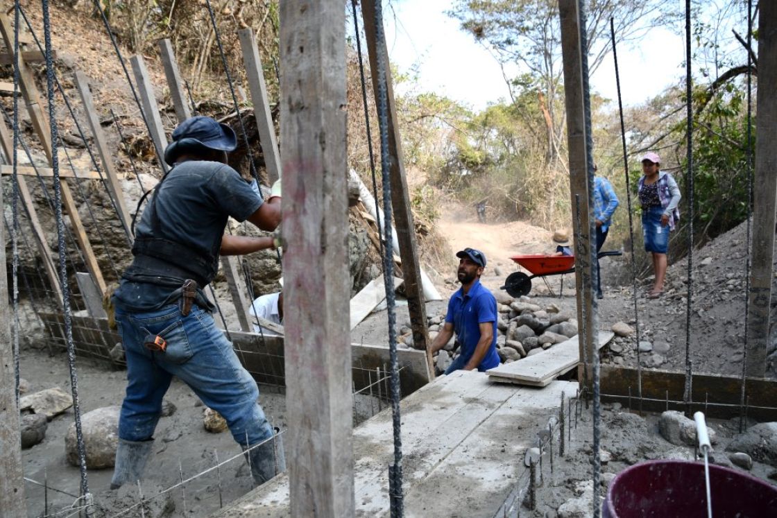 Eine Baustelle in einem trockenen Flussbett. Zwei Männer befestigen einen Holzpfosten im flüssigen Beton.