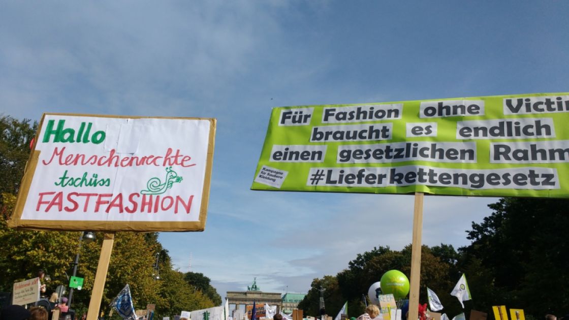 Protestschilder vor blauem Himmel. Im Hintergrund das Brandenburger Tor