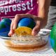 Eine halbe Pampelmuse, die außen wie eine Weltkugel angemalt ist, wird auf eine Zitronenpresse gelegt