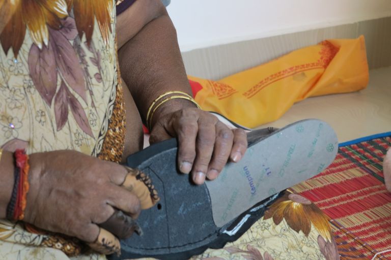 Eine Frau hat einen halbfertigen Schuh in der Hand. Drei Finger einer Hand sind mit einem Lederschutz überzogen.