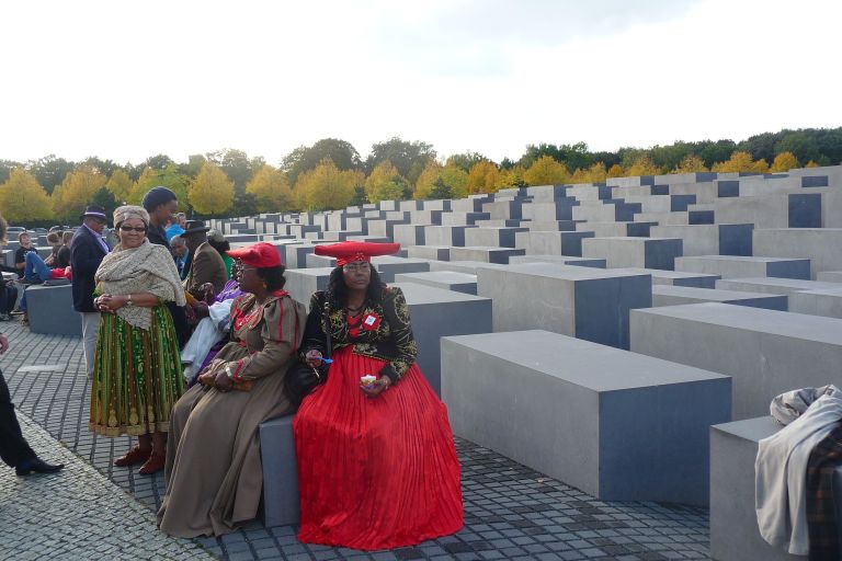 Frauen aus Namibia sitzen auf Stenen am Holocaust-Mahnmal in Berlin