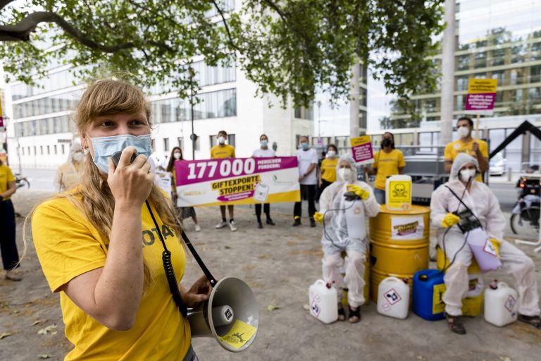Eine junge Frau mit Maske im Gesicht spricht durch ein Megafon. Sie ist Teil einer Protestgruppe.