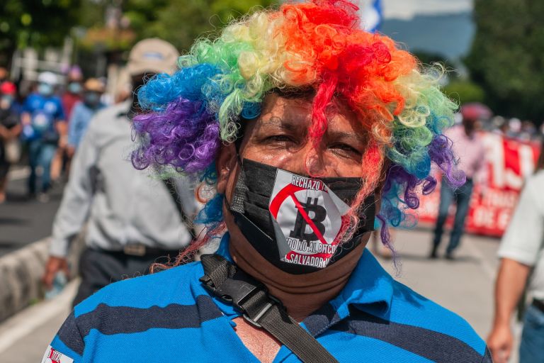 Mann mit Clownsperücke und Protestaufklebern auf seiner Kleidung