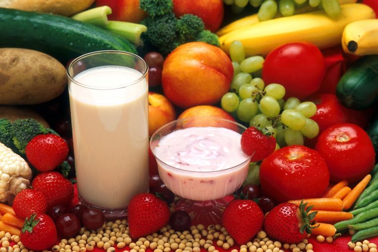 Frisches Obst und Gemüse, ein Milchglas, Joghurt und Kerne liegen dekorriert auf einem Tisch