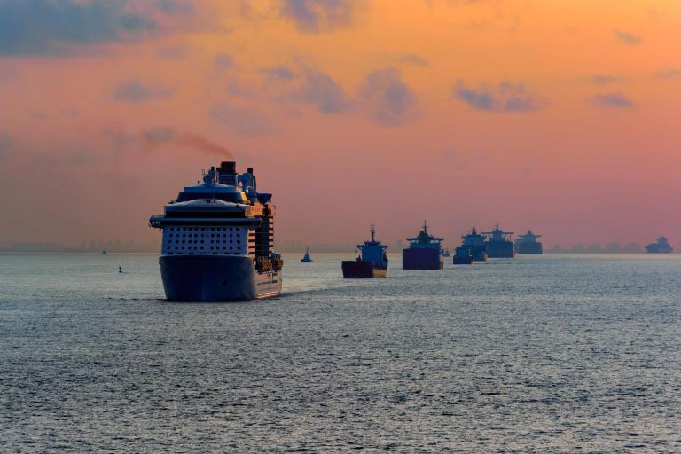 Ein großer Dampfer auf dem Meer, dahinter kleine Tanker. Am Horizont geht die Sonne unter.
