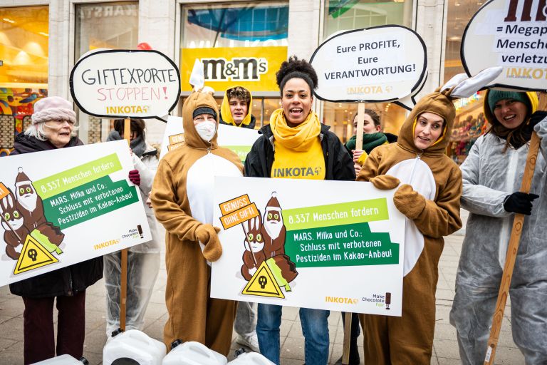 Mitarbeiter*nnen von INKOTA protestieren mit Schildern in der Hand vor einem Schokoladengeschäft