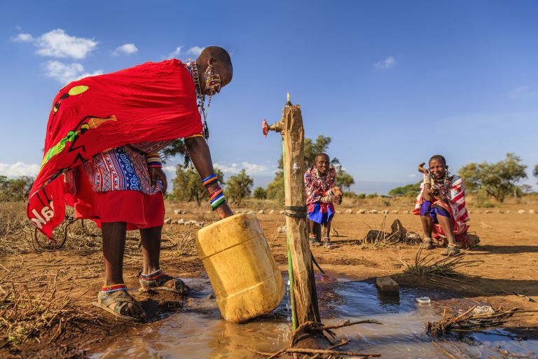 Eine Massai-Frau hebt einen großen Kanister an, der mit Wasser gefüllt ist