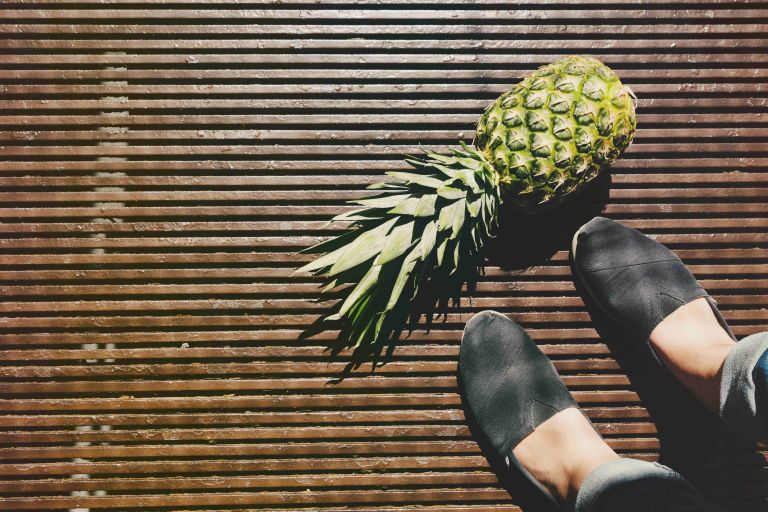 Eine Ananas liegt auf einem Holzfußboden und die Füße einer Person sind zu sehen