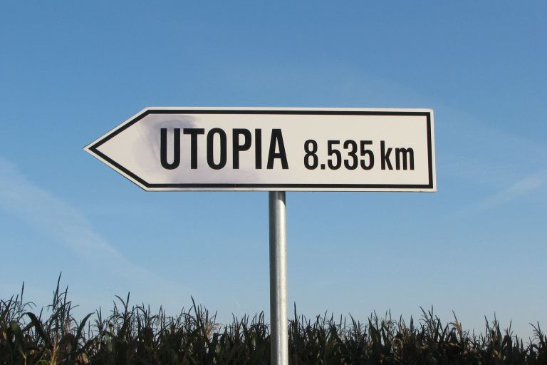 Grafik: auf einem realen Bild sieht man ein weißes Verkehrsschild in Form eines Richtungsanzeigers. Auf dem Schild steht das Wort Utopia und eine Kilometer-Angabe