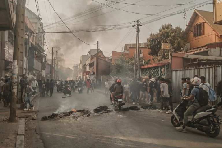 Foto einer brennenden Straßenblockade; viele junge Menschen auf der Straße